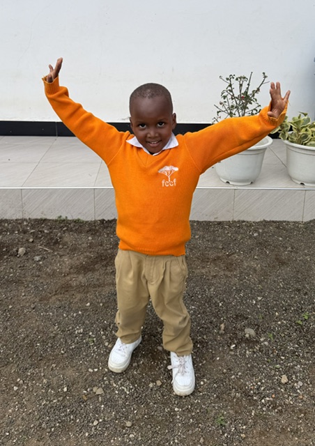Image of young school age boy smiling with arms raised in oragne sweater and khaki pants